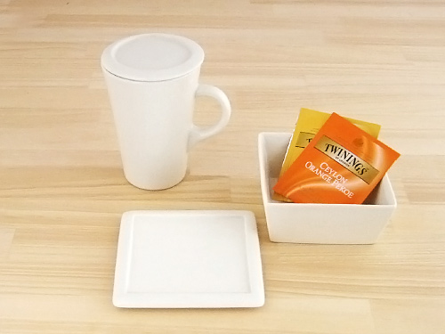 蓋付きのマグカップとティーカップトレイ、オレンジとイエローのパッケージのお茶がのっている。